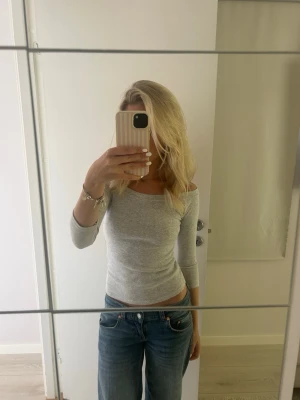 Ljusgrå offshoulder topp - Säljer en ljusgrå offshoulder topp med trekvartsärm. Toppen är tight och har en enkel, stilren design som passar perfekt till jeans eller kjol. 