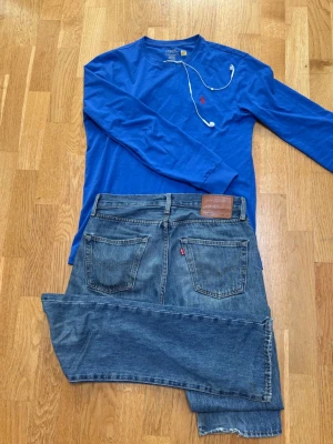 Levis 501 - Klassiska blå jeans från Levi's med rak passform och fem fickor. Jeansen har en vintage look med lätt slitna detaljer och Levi's ikoniska röda etikett på bakfickan. Perfekta för en avslappnad och tidlös stil. Storlek 29/32! 