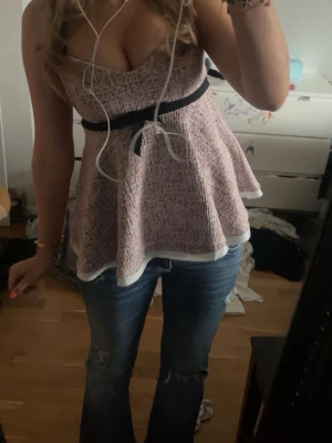 Rosa topp med svart rosett - Säljer en söt rosa topp från zara. Med svart band och rosett under bysten. Toppen har en utsvängd modell och vita kanter nertill. 