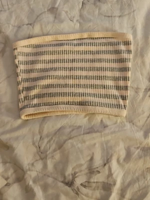 Randig tubtopp från FB Sister - Säljer en ribbad tubtopp från FB Sister i storlek XXS. Toppen har horisontella ränder i beige och grått, och är gjord i ett stretchigt material som sitter tajt. Perfekt att styla med jeans eller kjol för en trendig look.