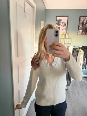 Beige stickad tröja med volangkant - Säljer en ljusbeige stickad tröja från Vila med lång ärm och v-ringning. Tröjan har en söt volangkant runt halsen och ribbade muddar vid ärmslut och nederkant. Perfekt för dig som gillar en enkel men ändå feminin stil. Jag säljer då den inte kommer till användning💕