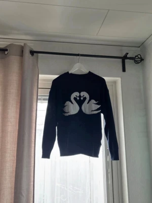 Mörkblå stickad tröja med svanar - Mysig mörkblå stickad tröja med två vita svanar som bildar ett hjärta på bröstet. Tröjan har rund halsringning och långa ärmar. Perfekt för dig som gillar djurmotiv och vill ha en unik look.🫶🏻🤍✨
