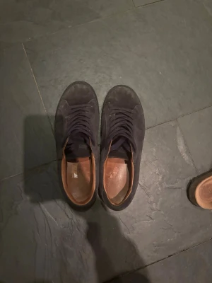Svarta låga sneakers i mocka - Snygga mörkblå sneakers i mocka med lågt skaft och matchande mörkblå skosnören. Insidan är fodrad i brunt läder vilket ger en schysst kontrast. Perfekta för dig som gillar en clean och stilren look.