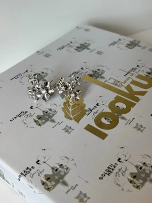 Ioaku le fleur örhängen  - Säljer ett par snygga örhängen i silverfärg med blommotiv. Örhängena har flera detaljerade blommor i olika storlekar och en glittrande mitt som ger extra effekt. Perfekta för dig som vill ha något unikt och trendigt till din stil. Och gjord i kirurgisk stål! 💕