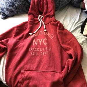 Röd hoodie med luva, ficka och tryck på framsidan av märket Premium Apparel i storlek M. Ganska stor dock så den passar även en storlek L.