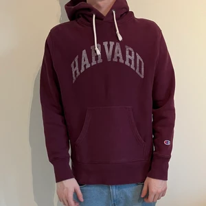 Champion hoodie. Storlek M.  - Vinröd champion hoodie med ett Harvard tryck över bröstet. Plagget har krympt lite i tvätten. Den är något tjockare. Tröjan är köpt i april 2021, original pris 1000kr. Tröjan är i väldigt bra skick, inga fläckar eller skador. 