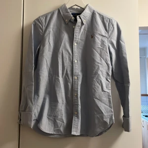Ralph Lauren skjorta  - En blå Ralph Lauren skjorta i storlek 16. (Som en Xs) använts en gång på en skolavslutning.