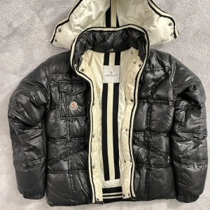 Moncler jacka - Säljer en äkta Moncler jacka i stl 2 (34). Jackan har knäppning framtill (ej blixtlås) och avtagbar huva. Använt men gott skick. Nyligen kemtvättad. 