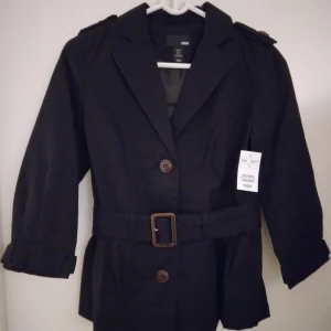 HELT NY & OANVÄND Svart kort jacka / safarijacka / cargojacka/ kavaj. Strlk: 34/XS. Felfri. - HELT NY & OANVÄND Svart kort jacka / kavaj, perfekt för våren och sommaren. Stängs med knappar och har skärp i midjan. Strlk: 34/XS.  Material: Kraftigare bomull, foder i satin. Helt felfri. Tags/lappar sitter kvar sedan inköpet. Nypris i butik 298 kr.
