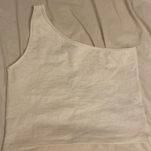 Crop-top med ett band  - En fin vit crop-top med ett axelband. Perfekt för sommaren. Den är både stretchig och skön att ha på sig. Säljer för den är för stor för mig 