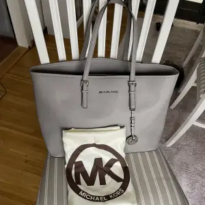 En medelstor grå Michael Kors Jet Set Leather bag från 2019 i fint skick. Väskans handtag är lite smått slitna men utöver det är väskan i väldigt bra skick. Detaljbilder finns om så önskas! Förvaringspåse från MK ingår. 