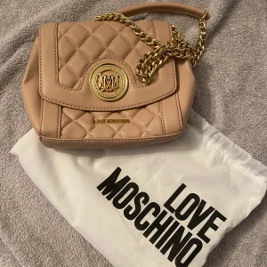 ÄKTA Moschino väska - Ny handväska med axelrem i gulddetaljer. Äkta!!   Puderrosa superfin men kommer tyvärr inte till användning här. Dusstbag ingår 