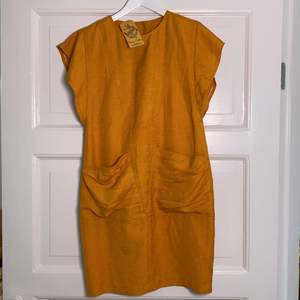 Senapsgul/orange klänning med fickor. Inköpt på Beyond Retro men aldrig använd. Har inbyggd ”underklänning”. Står ingen storlek men är ett mellanläge av S och M enligt mig. Har små axelklaffar. 