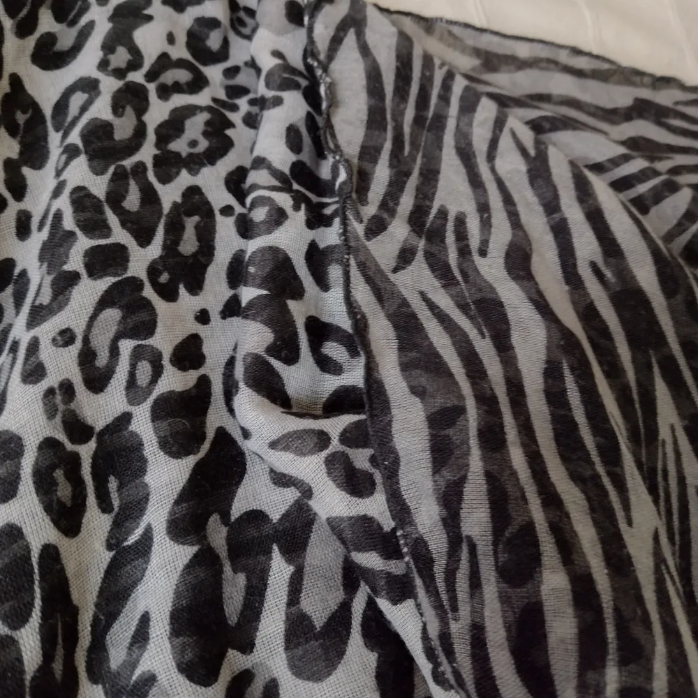 Lång grå/svart djurmönstrad sjal. Olika mönster på fram- och baksida. Nästan 2 m lång och 70 cm bred. Några dragna trådar. Tunn och lätt.. Accessoarer.