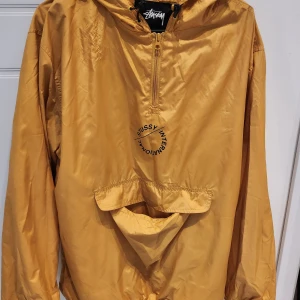 Stussy Nylon pop over jacket M - Säljer denna för en symbolisk summa då jag ska flytta och inte vill slänga den. Kardborren från fickan har lossnat men den sys på enkelt igen. Nypris 1600:- Kan skickas mot porto på 66:- eller hämtas i Stockholm.