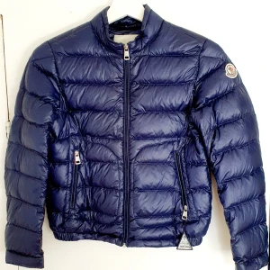 Moncler - Moncler jacka i storlek 140 (ca 10 år). Supermjuk, lite tunnare dunjacka. Mycket bra skick, dock finns det spår av användning, bl a så är tryckknapparna vid ärmslut lite slitna. 