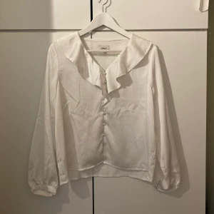 Vit sidenblus - Elegant sidenblus från Only i storlek M. Använd vid ett tillfälle. Fin volang med knappar. Kan mötas upp i Sthlm eller skickas mot fraktkostnad.
