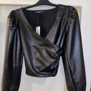 Skinn topp - Topp i fejk läder/skinn. Köpt på bikbok. Aldrig använd sitter fortfarande prislapp kvar. Köpt för 399kr. Säljer den pga för liten. Tajt i midjan och vida ärmar har även en dragkedja för att enklare få på. 