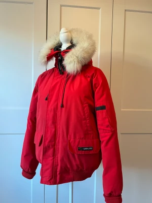Canada Goose jacka röd stl. M - Säljer min härliga jacka Canada Goose jacka röd stl. M. Välanvänd jacka av tidig modell. I övrigt hel och ren. En liten fläck på sidan som ej syns. Äkta pälskrage. 