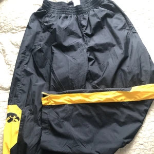 Svarta och gula trackpants från Nike  - Svarta täckliknande byxor med gula ditaljer. Materialet liknar en vindjackas material.