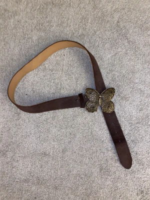 Skärp med fjäril  - Snyggt skärp i läder! Måttet till det första hålet är 76,5 och 101cm till de längst ut, går såklart att göra fler egna hål! 