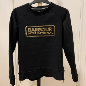 Barbour tröja - Väldigt fin Barbour tröja i storlek XS, passar XS-M. Guldkedja med Barbour märket vid midjan på båda sidorna av tröjan. Knappt använd, endast enstaka gånger. Nyskick. 