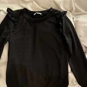 Svart tröja med volanger - Bra skick. Storlek M men passar även S. Volanger på axlarna. Jättefin men kommer inte till någon användning. Köpare står för frakt. Skriv privat vid intresse💞