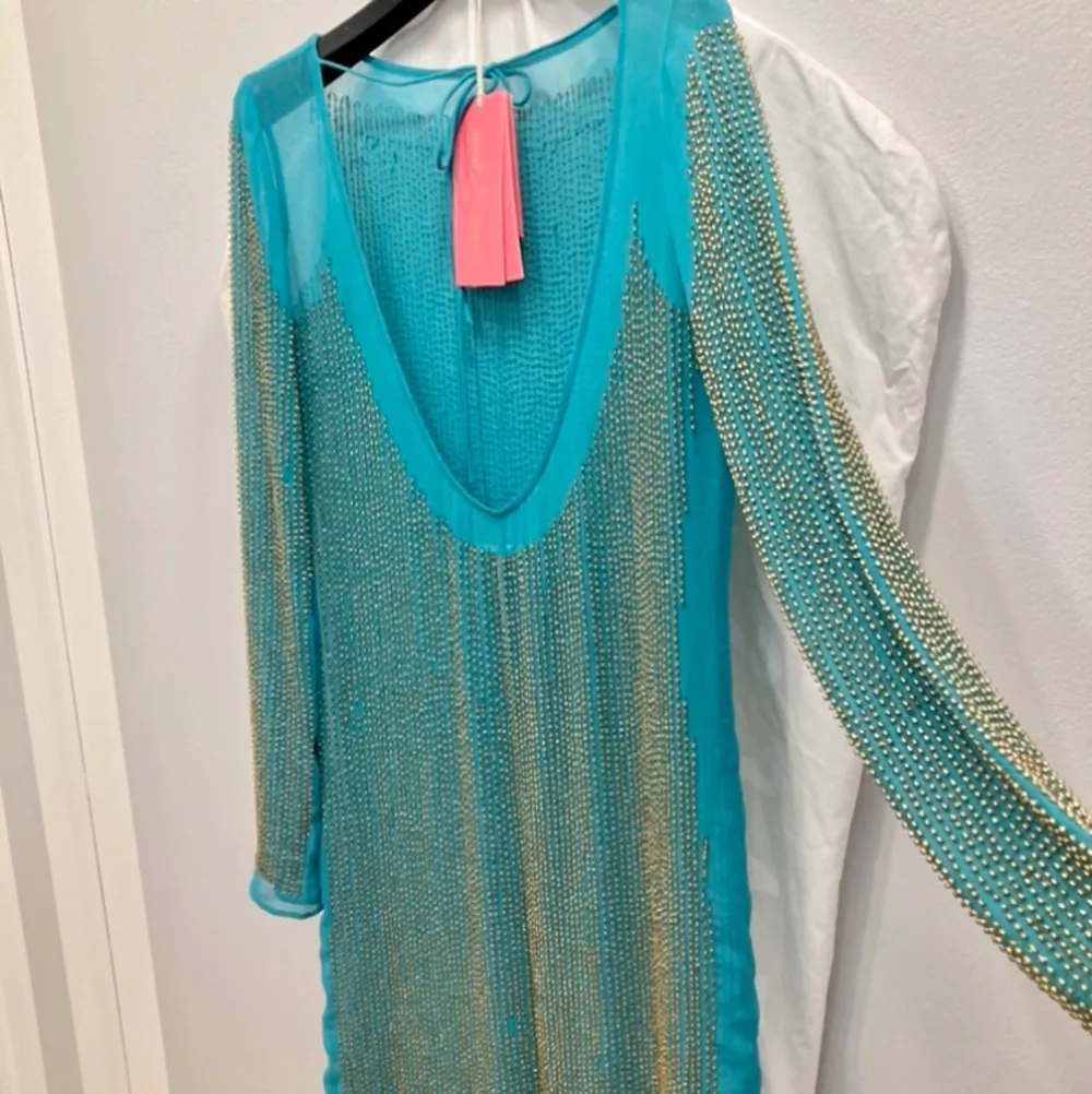 Superfin klänning från Needle & Thread som aldrig hunnit bli använd.  Är i nyskick och är handsydda pärlor i guld, samt en låg rygg med snören som man kan knyta upptill.  Skulle säga att färgen är blå,grön eller en väldigt ljus petrol. . Klänningar.