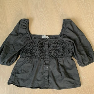 Svart topp NAKD - Svart topp från Nakd med knappar och puffärmar. Storlek 38