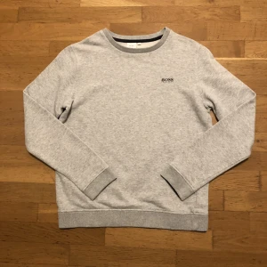 Sweatshirt HUGO BOSS, stl 14-S - Sweatshirt från Hugo Boss, stl 14-S, ljusgrå melerad med mörkblått tryck. Bra begagnat skick. Kommer från rök- och djurfritt hem. 