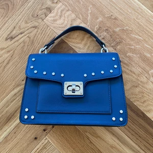 Blå handväska - Säljer denna jättegulliga blå väska med silvriga nitar. Vet tyvärr inte märket (har glömt)… bra skick, använd max 10 gånger. Tillhör en matchande scarf.