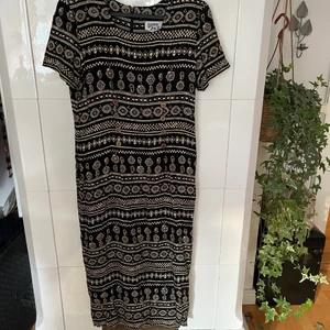 Mönstrad Svart Klänning - 90 tals klänning med knytning baktill och träknapp detaljer framtill. Aclarna har en mindre vaddering som get klänningen en super fin passform på. 