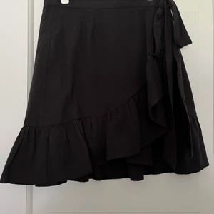 Svart kjol med volanger storlek 32 - Svart kjolens volanger, samt knytning och rosett i midjan. Passar lika bra på sommaren som på hösten. 