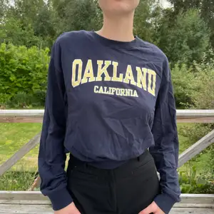 Mörkblå collegetröja från HM. På tröjan står det ”Oakland, California”