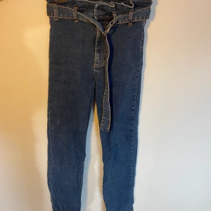 Blåa jeans - Blåa jeans med band som skärp i midja, högmidjade, vintage style. Tyvärr är märket borta så vi kan inte skriva vart dom är ifrån.