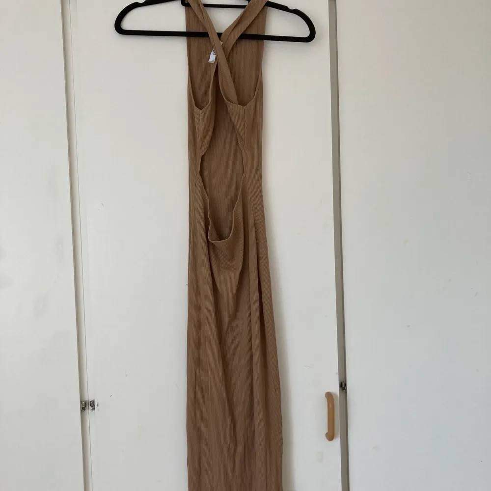Lång brun klänning med öppen rygg, från NA-KD. Klänningen har två band som korsas och bildar en öppen rygg.. Klänningar.