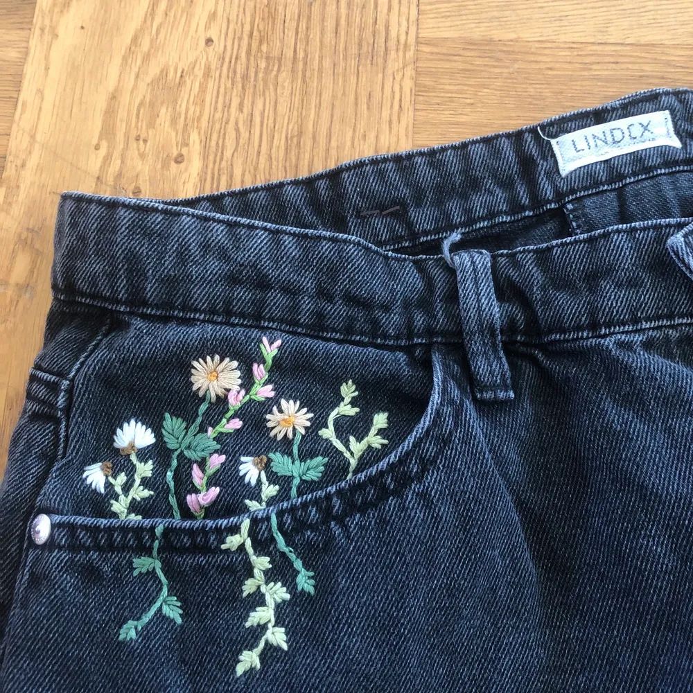 Svarta högmidjade jeans från Lindex med blommor i olika färger broderade på fickorna. Långa i benen. Storlek 44 men är lite baggy i modellen.. Jeans & Byxor.