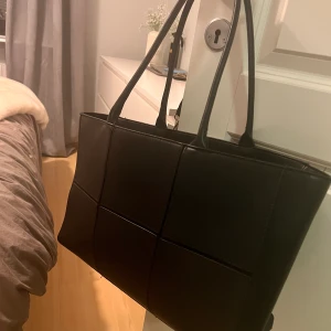 Svart väska  - Svart mönstrad väska, 40x20 cm. Finns två fack i väskan. 