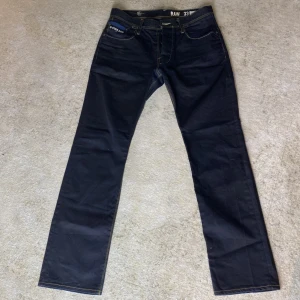 G-star Raw Jeans Herr - Dessa jeans är vaxade, vilket betyder att dom är lite hårda i materialet! Dock väldigt komfortabla och av högsta kvalité, slitstarka! Raka vid foten, inga slitage. Fina sömmar i designen. Även blå detalj på bakfickorna. Väldigt gott skick!!