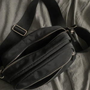 Axelremsväska  - Svart axelremsväska med justerbar axelband och har 2 fack med dragkedja. 50kr +frakt