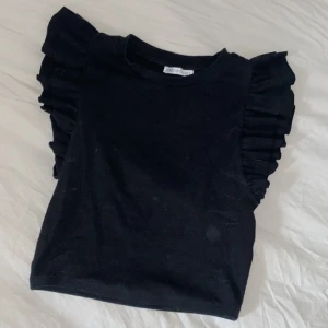 Volangtopp Zara  - En jättefin svart trendig volangtopp från Zara. Knappt använd. Köptes nyligen. I mycket bra skick! Storlek M men den är liten i storleken. Skulle säga att det är som S/XS