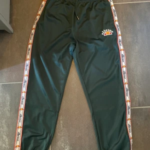 Ellesse trackpants - Snygga byxor från Ellesse med logga längs benen. Går att knäppa upp då det finns knappar längs benen också! Sparsamt använda. Strl L men passar även M🔥