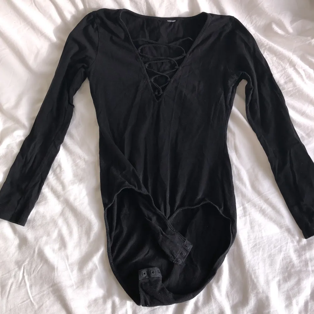 Svart långärmad bodysuit med banddetalj och djup V. Sitter jättebra, och går även att ha på baklänges för en hög krage och ryggdetalj!!  💥FÅ 50% AV 1 VARA OM DU KÖPER 2!💥. Toppar.