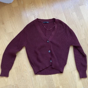 Cardigan med knappar - Denna superträndiga koftan är vinröd med svart/bruna knappar, så snygg till ett par gråa jeans! 