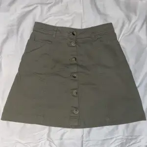 Olivgrön jeans kjol med bruna knappar från H&M. Storlek 34. Har inga bilder med den på då den är alldeles för liten. Aldrig använd.