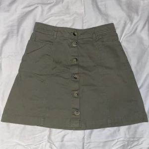 Olivgrön kjol - Olivgrön jeans kjol med bruna knappar från H&M. Storlek 34. Har inga bilder med den på då den är alldeles för liten. Aldrig använd.