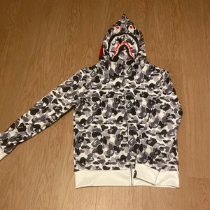 Bape zip up hoodie - En riktigt snygg bape hoodie som är grå,svart och vit. Den är använd bara 1 gång. Den är i jättebra skick och inga skador eller märken på hoodien. Säljer då den är lite för stor för mig.