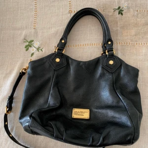 Marc Jacobs väska i skinn - Marc by Marc Jacobs handväska i svart skinn! Legat i min garderob de senaste åren, är i gott skick, inget sprucket skinn. Har en lång justerbar axelrem som är avtagbar. Ej byte!