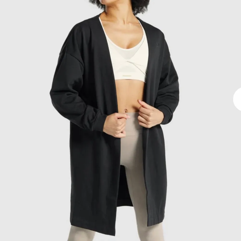 Whitney Oversized Robe i svart från Gymshark i storlek XS. Modellen från hemsidan har S på sig. Fint skick då den bara är använd ett fåtal gånger och den sitter oversized. Nypris: 599kr, mitt pris 300kr plus spårbar frakt på 66kr🖤. Tröjor & Koftor.