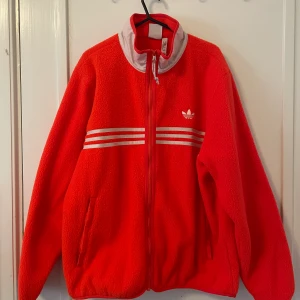 Adidas sherpa oversize-jacka - Orange jacka från adidas som aldrig använts. De vita strecken samt den vita kragen är i reflex-material. Supersnygg är den, bara inte på mig. 